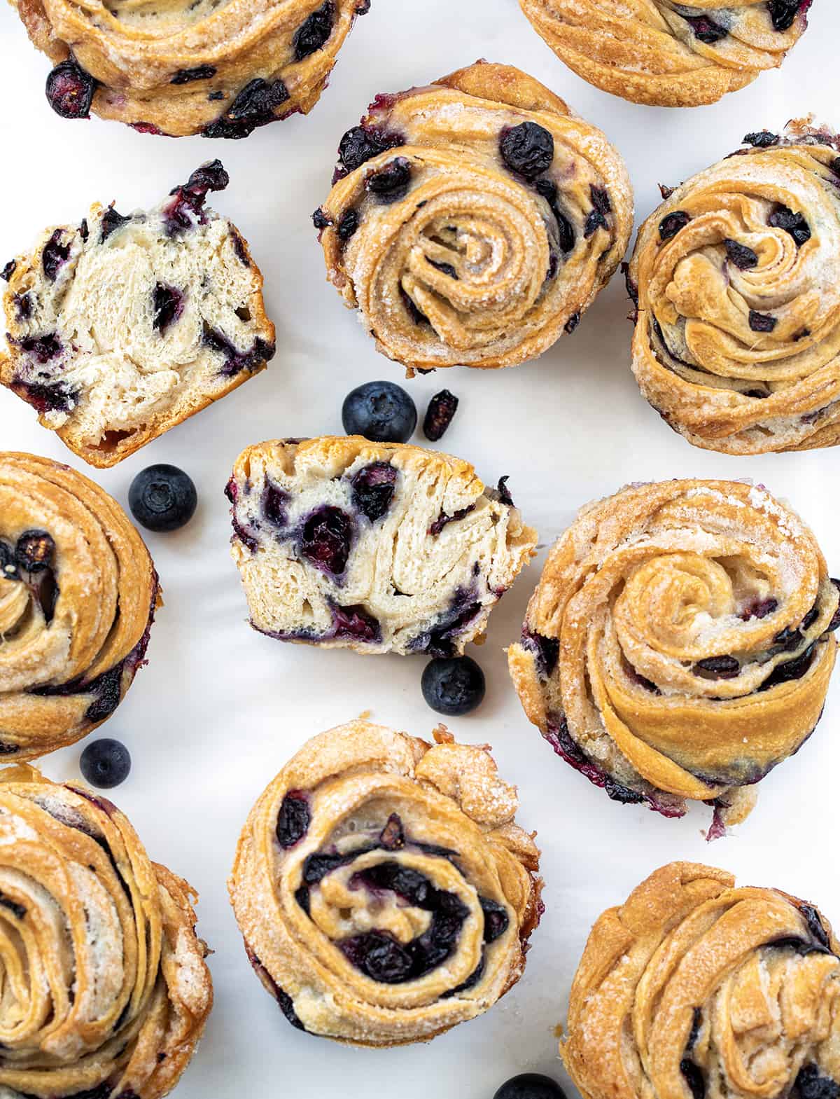 Blueberry Cruffins on a White Counter with Most Whole and One Cut in Half.