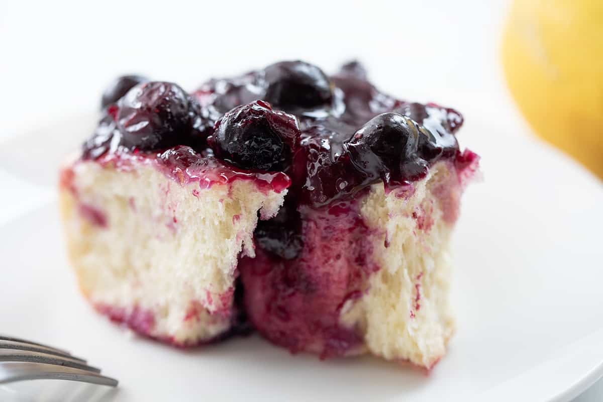 One Blueberry Lemon Skillet Roll on a White Plate with a Lemon in the Background.