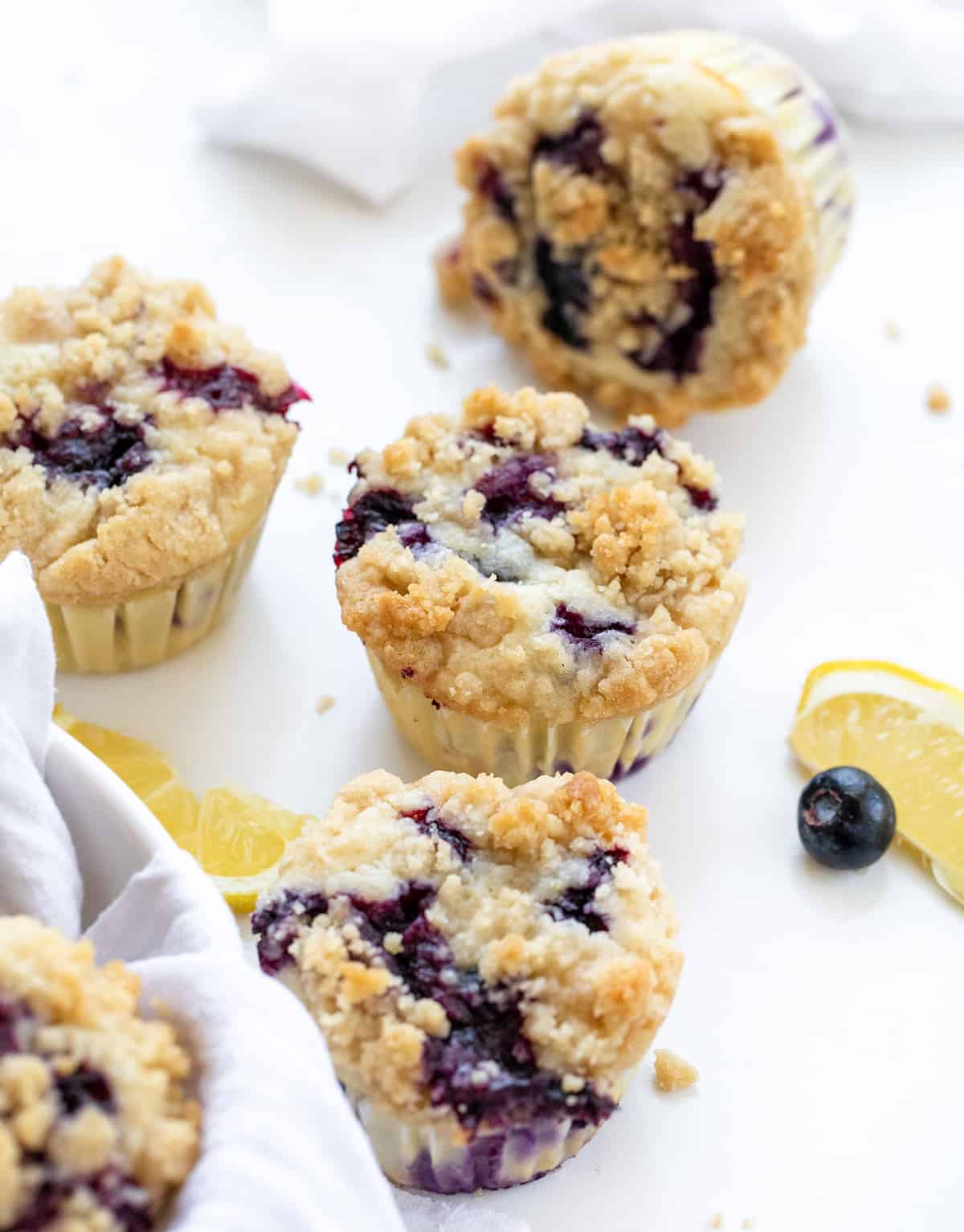 Blueberry Lemon Muffins on a White Counter with Fresh Lemon Slice and Blueberries.