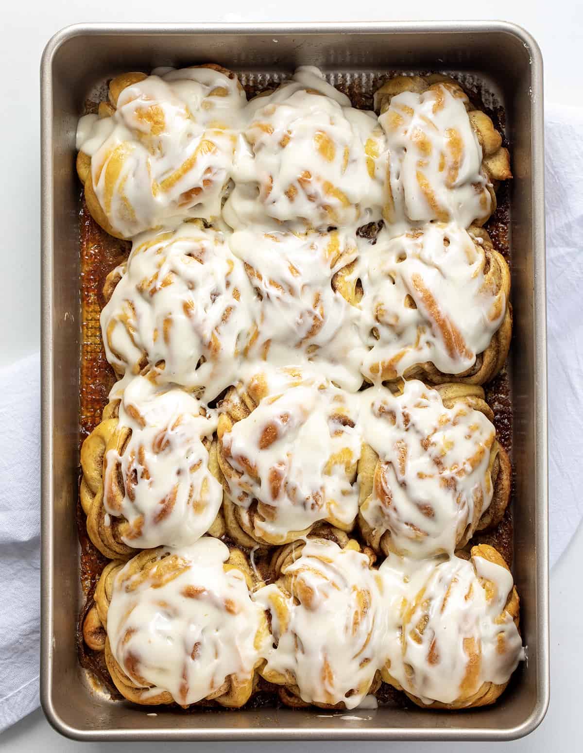 Frosted Braided Cinnamon Rolls in a Pan on a White Counter from Overhead.