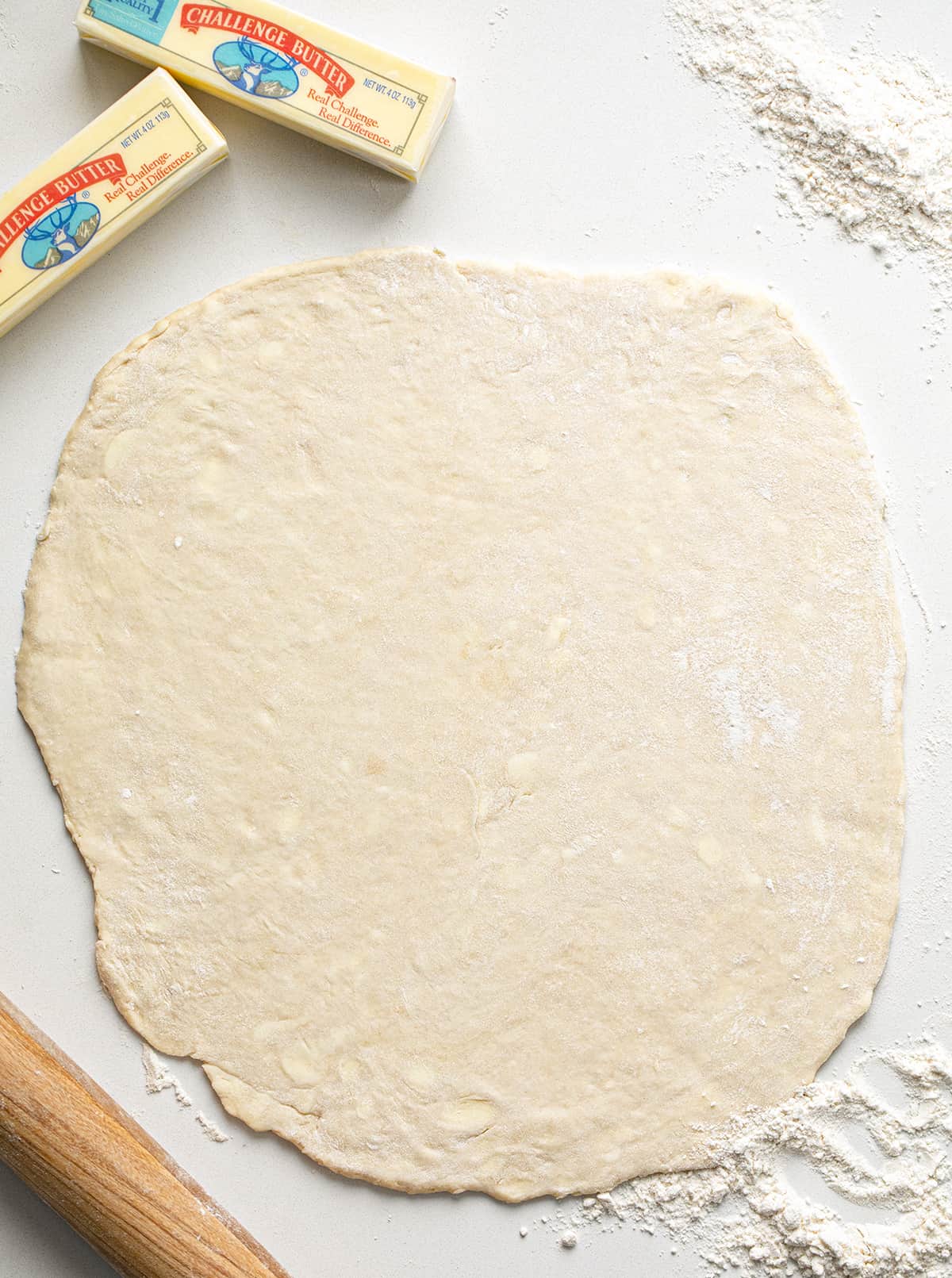 All Butter Pie Dough Rolled Out on a Counter with Butter, a Rolling Pin, and Flour Next to It.