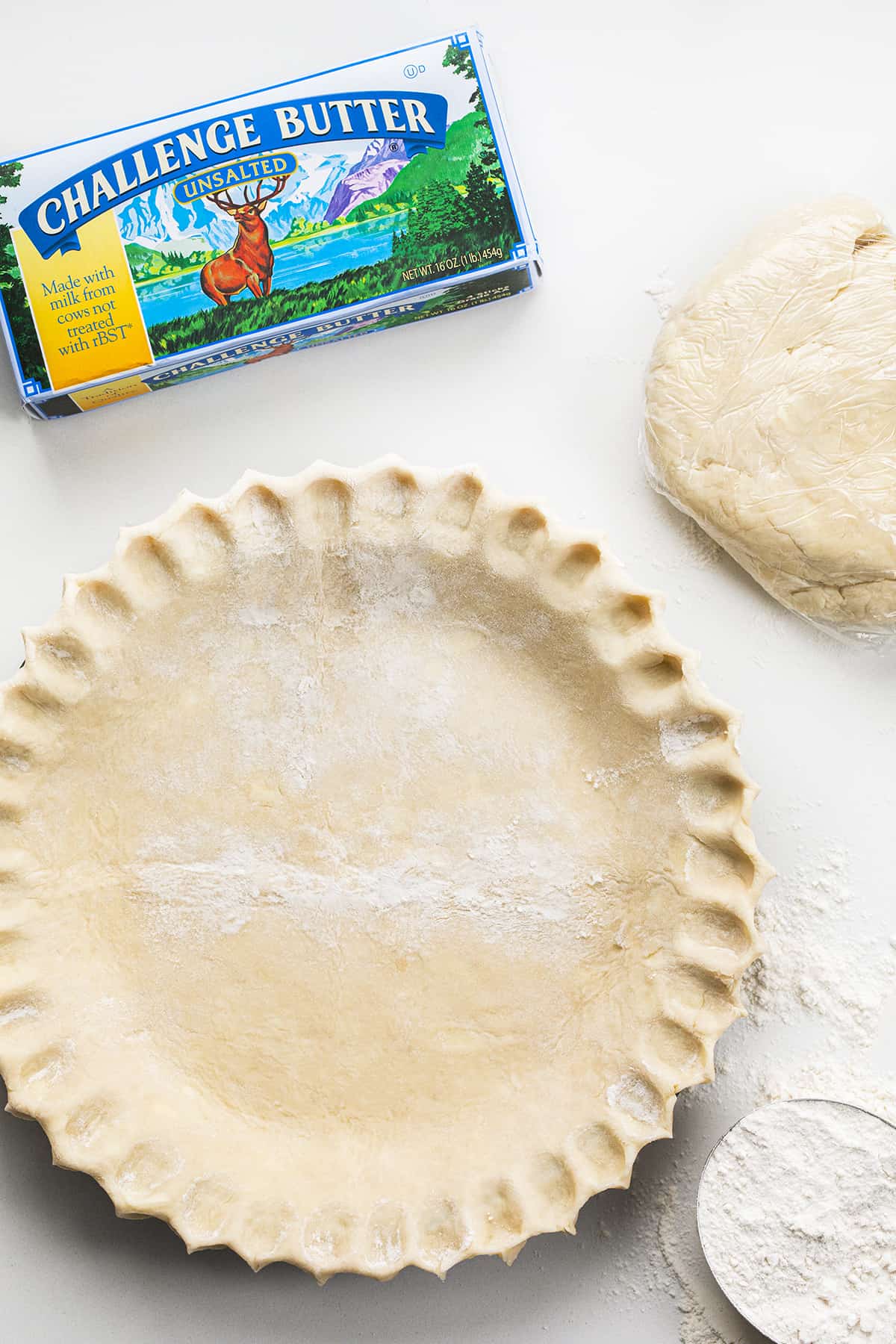 Pie Crust in a Pie that has Been Crimped Before Baking Next to Flour, Butter, and an Additional Pie Crust in Plastic Wrap. 