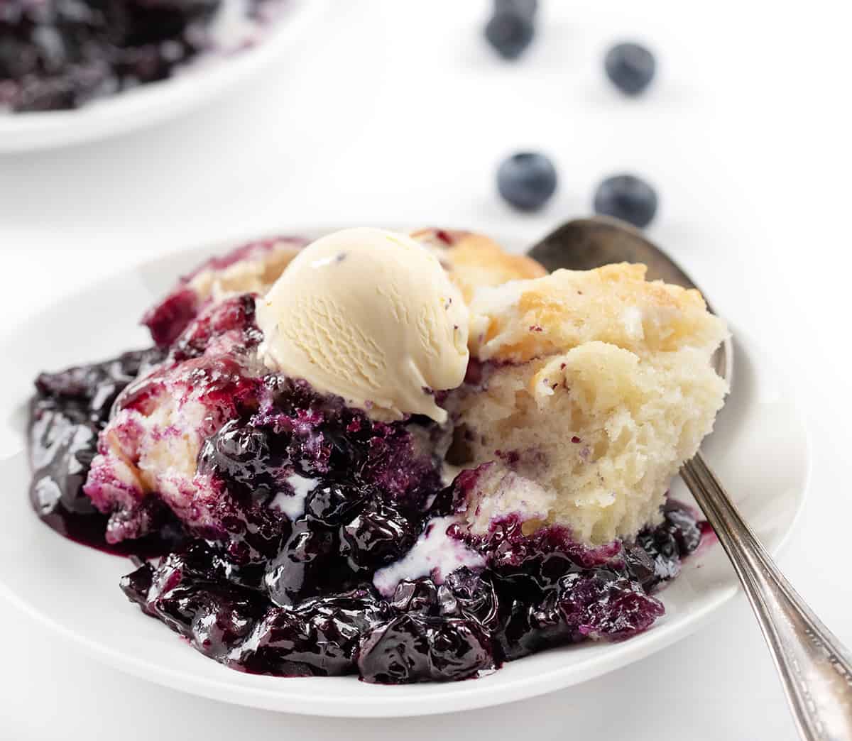 Plate of Butter Swim Biscuit Blueberry Cobbler on a White Counter with Blueberries.