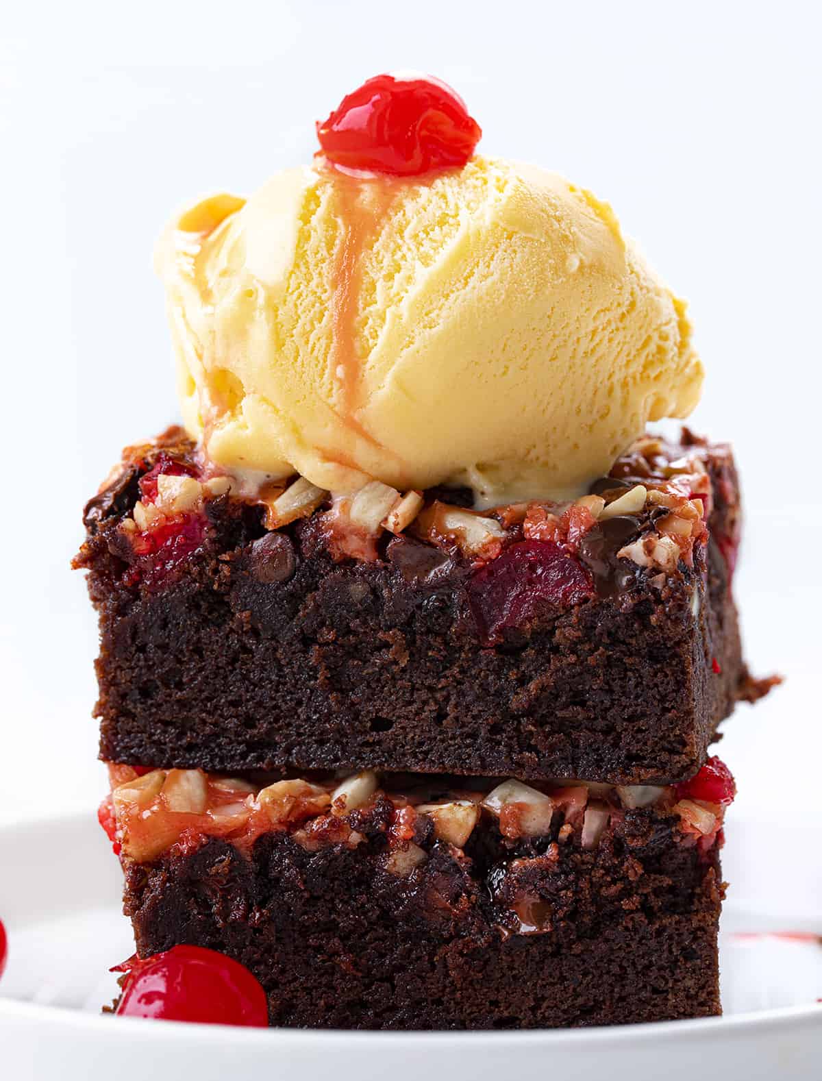 Stack of Cherry Chocolate Magic Brownies on a Plate with Ice Cream and a Cherry on Top.