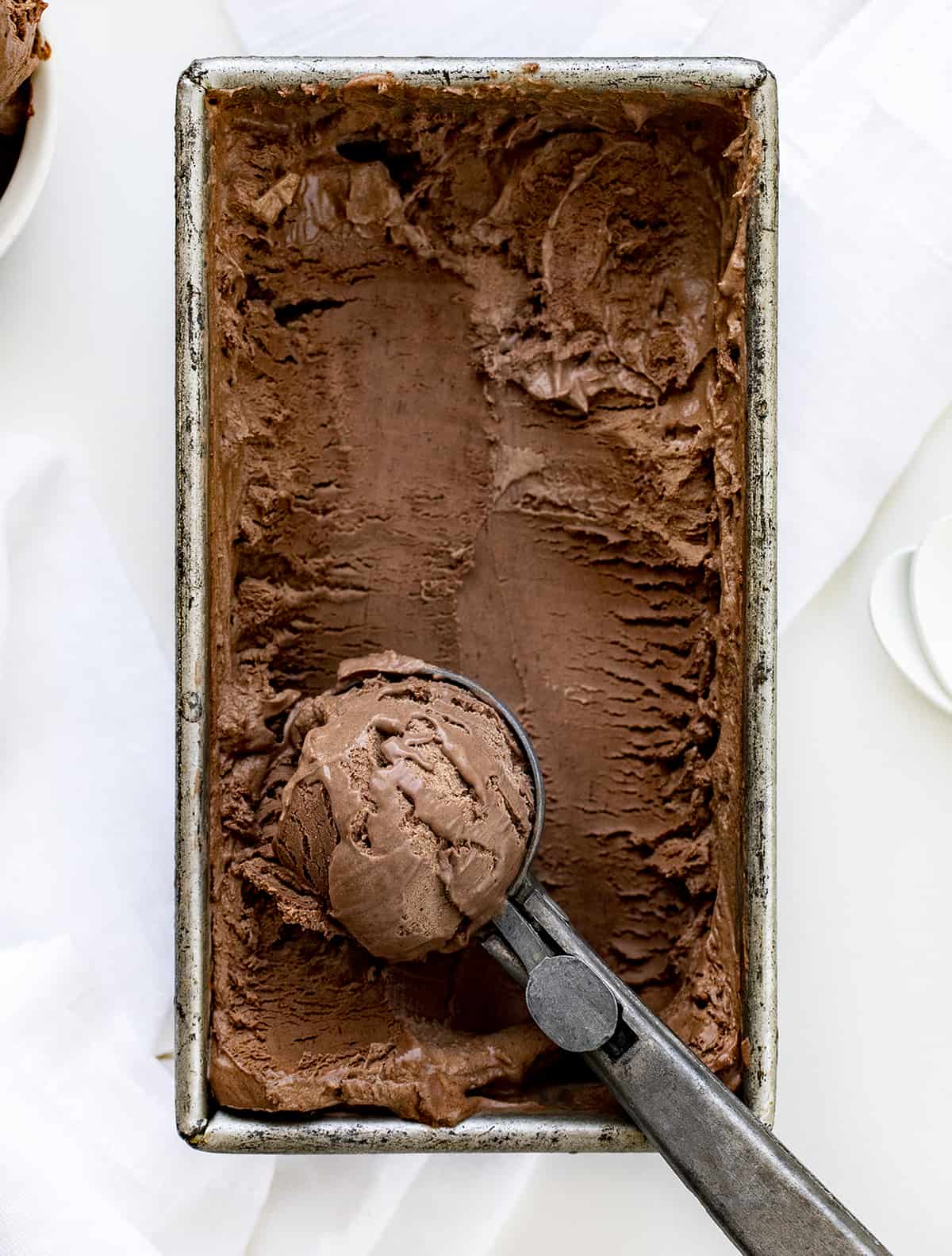 Pan of frozen No-Churn Chocolate Ice Cream on a White Counter with Scoop Full of Ice Cream from Overhead.