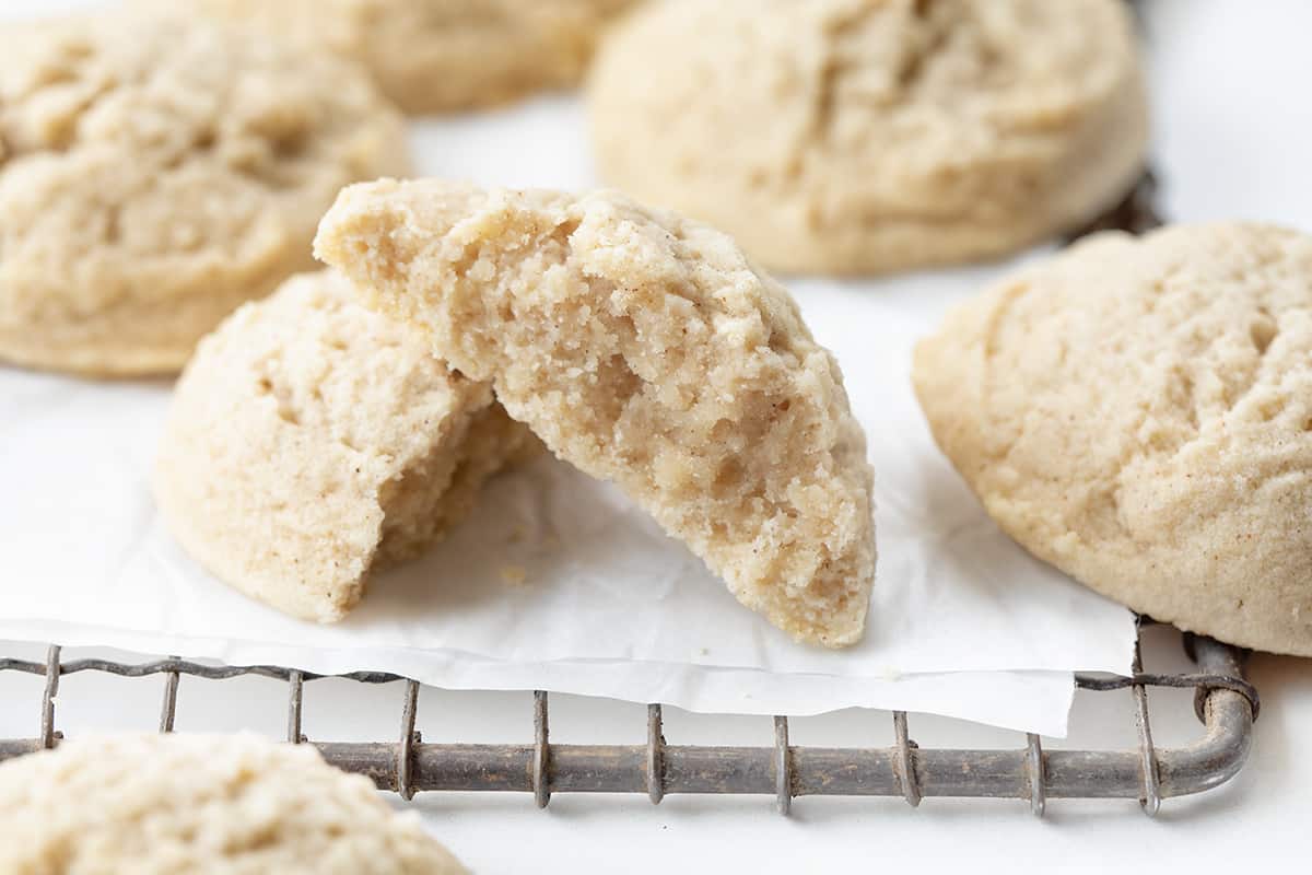 Cinnamon Butter Cookies on a Cooling Rack with Parchment and a Cookie Halved Showing Inside Texture.
