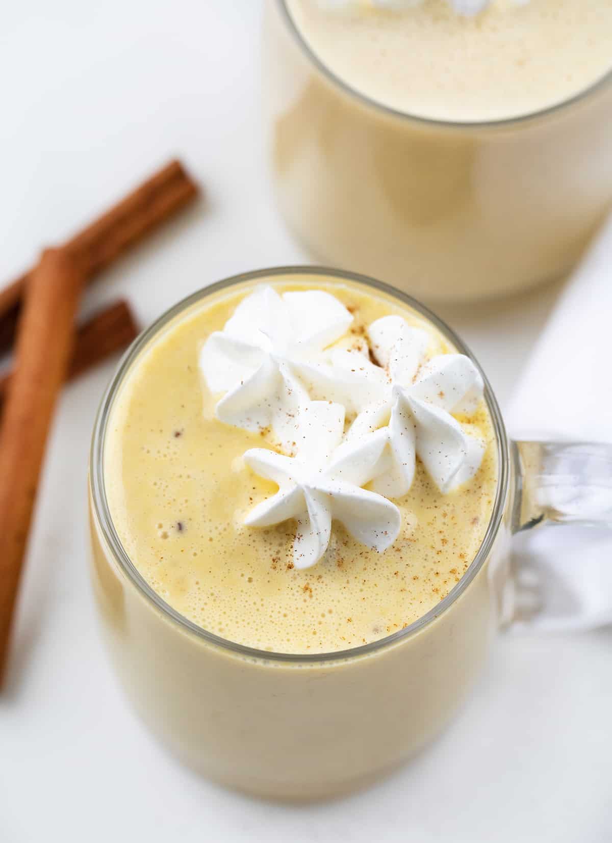 Glass mugs filled with eggnog and topped with whipped cream.