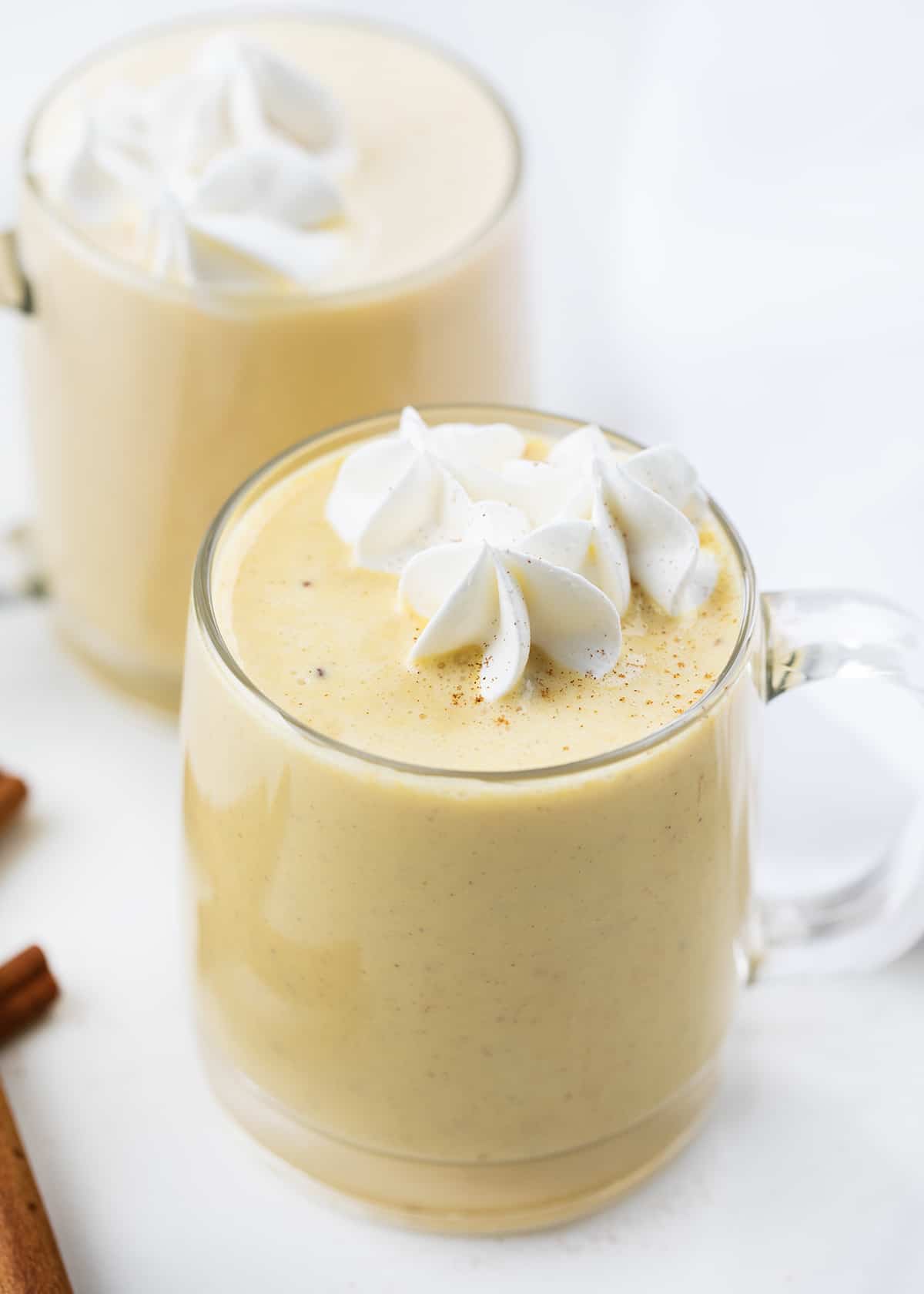 Glass mugs filled with eggnog and topped with whipped cream.