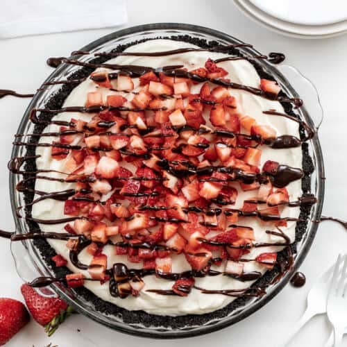 Overhead of a Chocolate Strawberry Marshmallow Pie on a White Counter with Hot Fudge Drizzle and Strawberries.