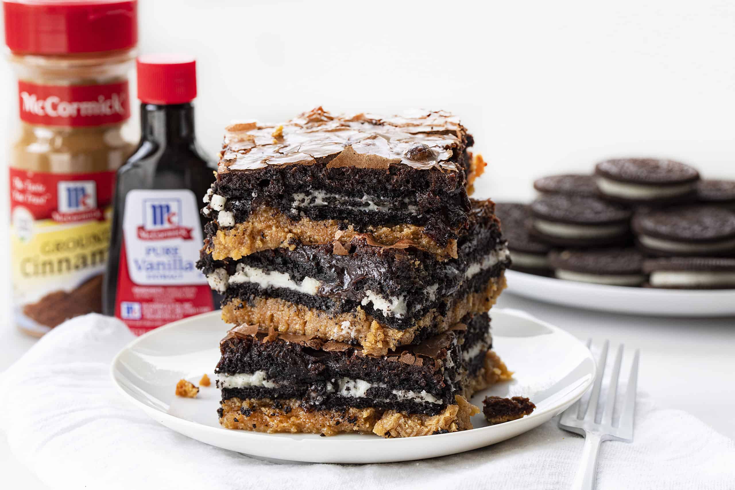 Stack of Peanut Butter Slutty Brownies with Oreos and Vanilla and Cinnamon in the Background