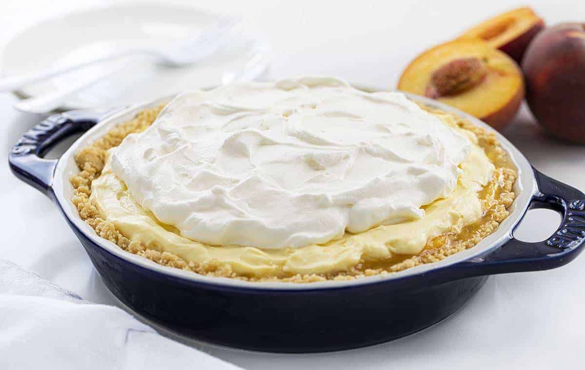 Peaches and Cream Pie in a Blue Pie Dish with Peaches in Back.