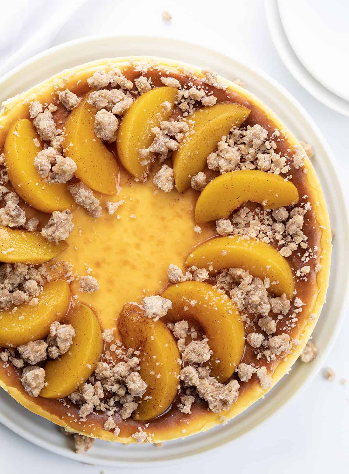 Looking Down on a Peach Crumble Cheesecake on a White Counter with Towel and Plates.