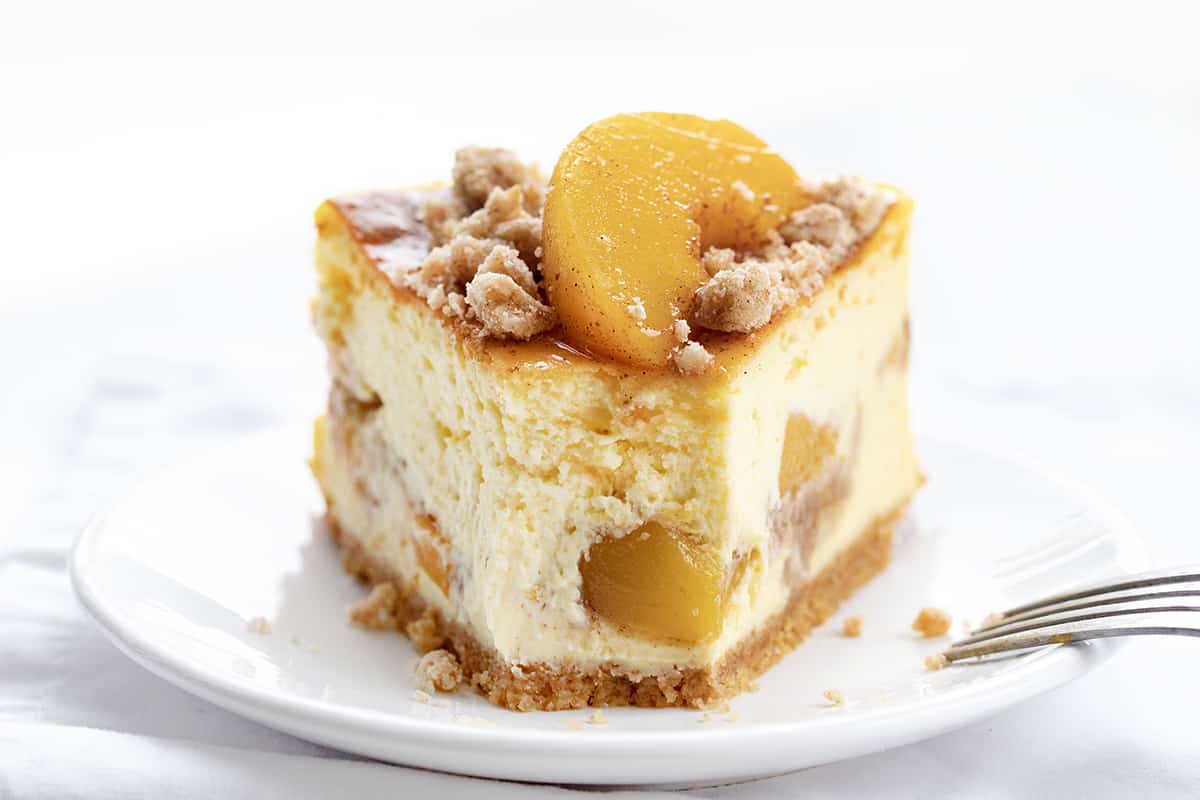 Piece of Peach Crumble Cheesecake on a White Plate with a Bite Removed.