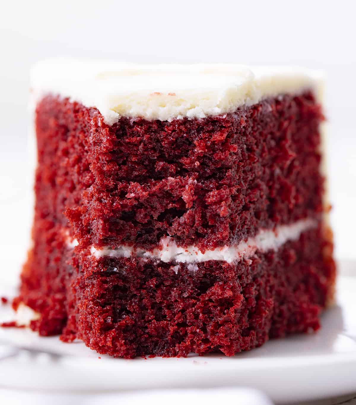Piece of red velvet cake on a plate with a bite removed.