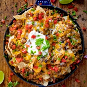 A Skillet Filled with Layers of Beef Nachos and Topped with Melted Cheese, Tomato, Sour Cream, and Lime.