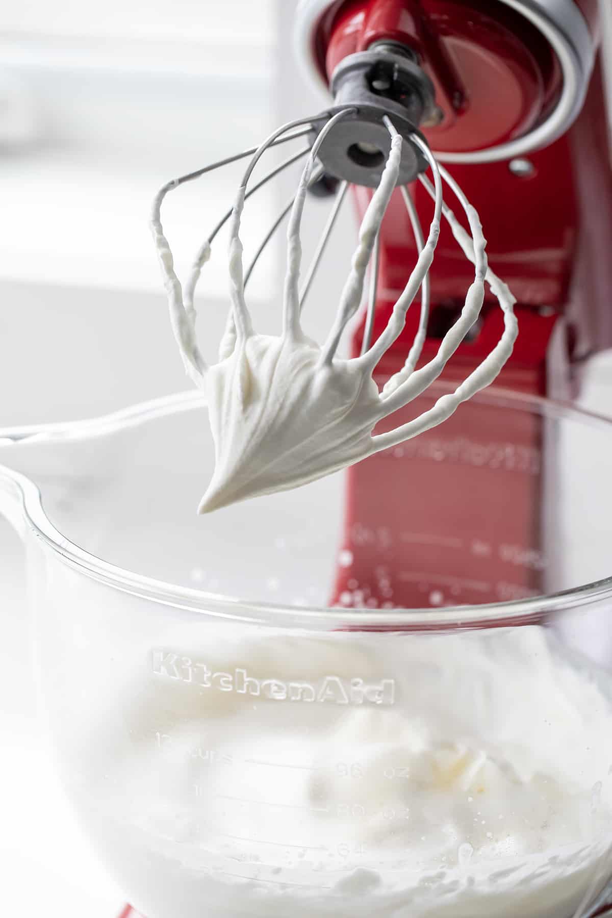 Mixer with whisk attachment with whipped cream on it, showing the stiff peaks.