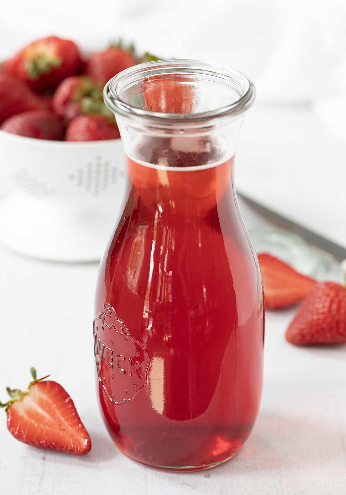 Bottle of Strawberry Simple Syrup Surrounded by Strawberries.