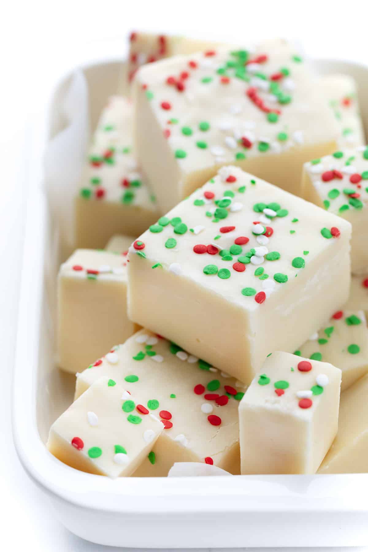 Pieces of Sugar Cookie Fudge that has green and red sprinkles in a dish. 